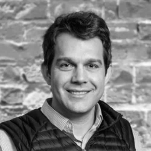 Professional headshot of Matthew Melville, a corporate and finance attorney, smiling in front of a brick wall background.